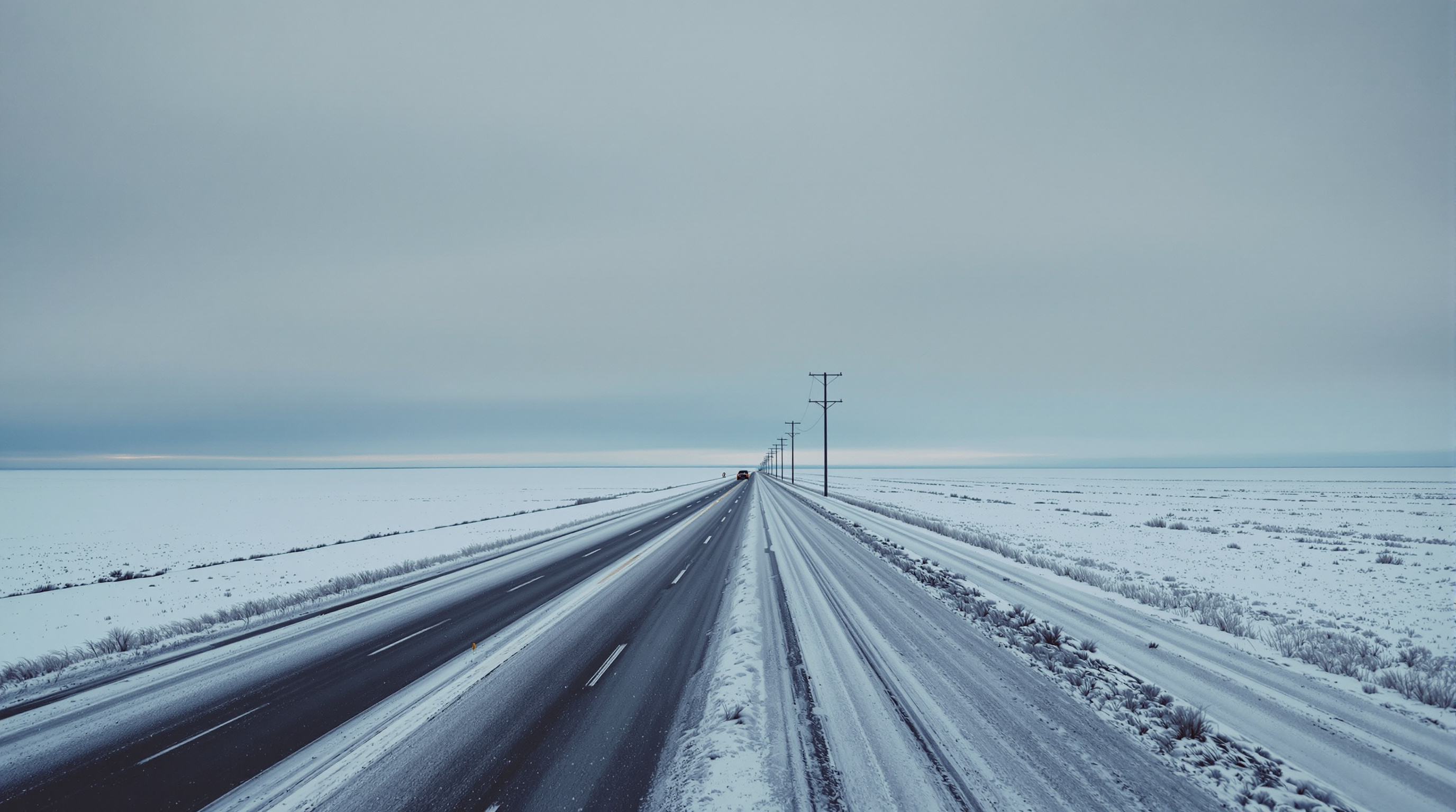 Vast snow-covered Midwestern plain with a lone highway and telephone poles under an overcast sky