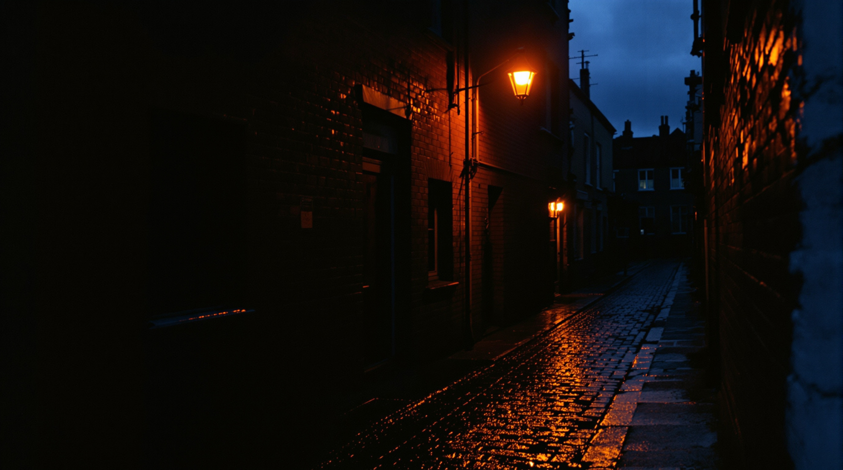 Moody urban alley at dusk with wet pavement and an orange streetlight, evoking 1990s British grit